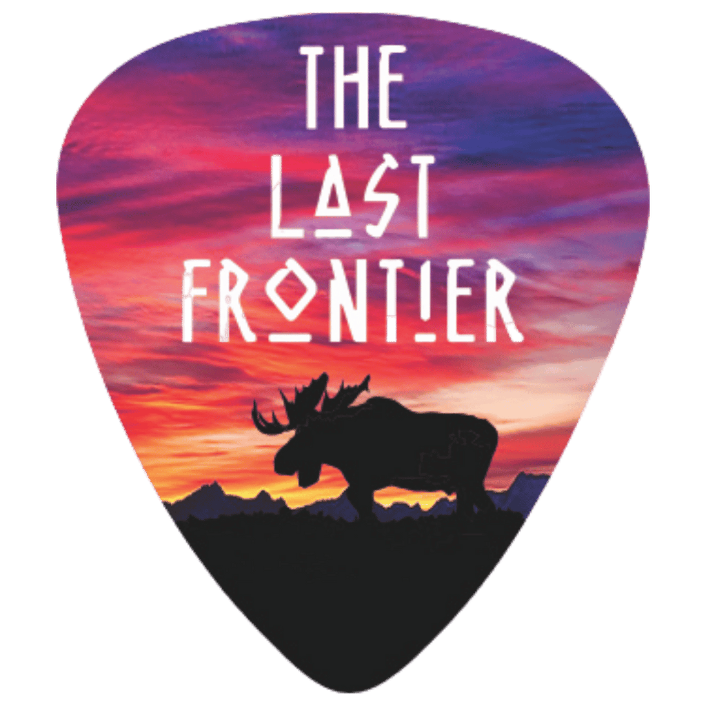 A guitar pick featuring a colorful sunset landscape design with the text 'THE LAST FRONTIER' and a black moose silhouette over mountains.