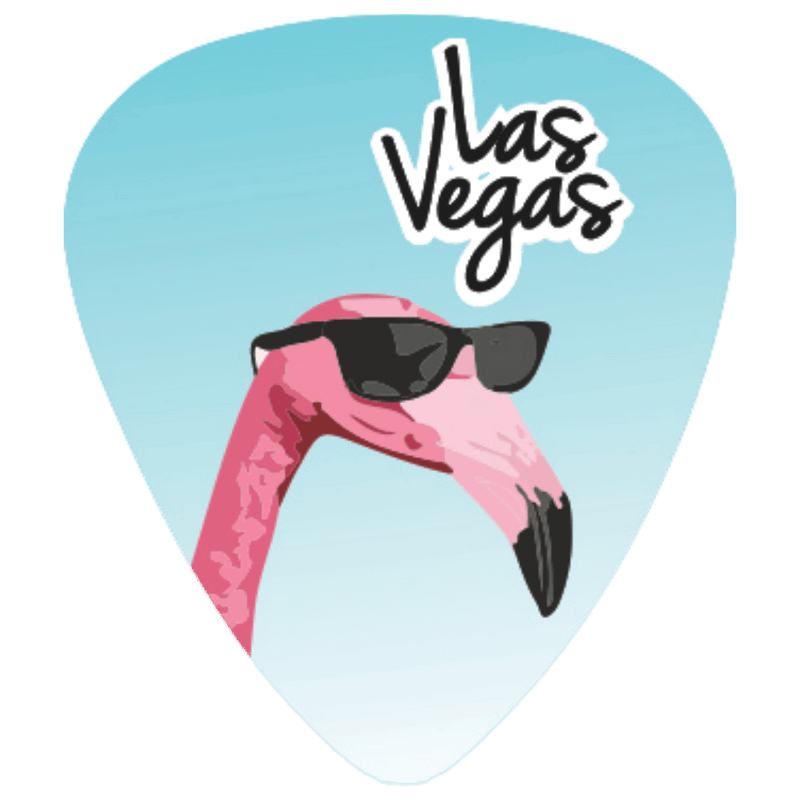 A guitar pick featuring a pink flamingo wearing black sunglasses against a light blue gradient background, with the words 'Las Vegas' in black script and white outline near the top.